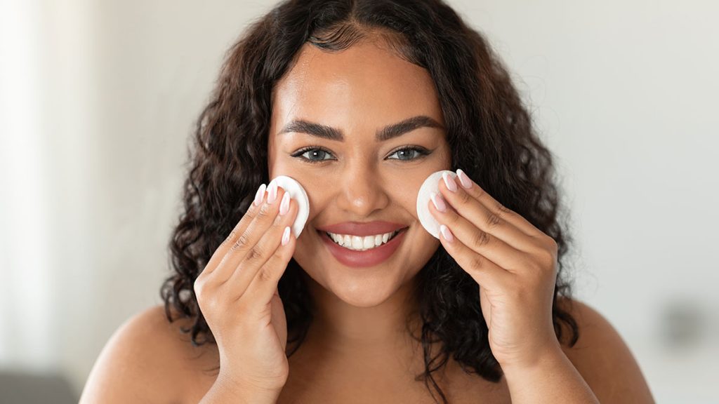 Facial skincare. Happy black woman cleansing skin with cotton pads and smiling